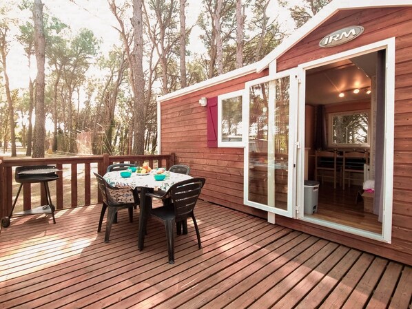 A wooden deck with a table and chairs, a grill, and a building with a sliding door.