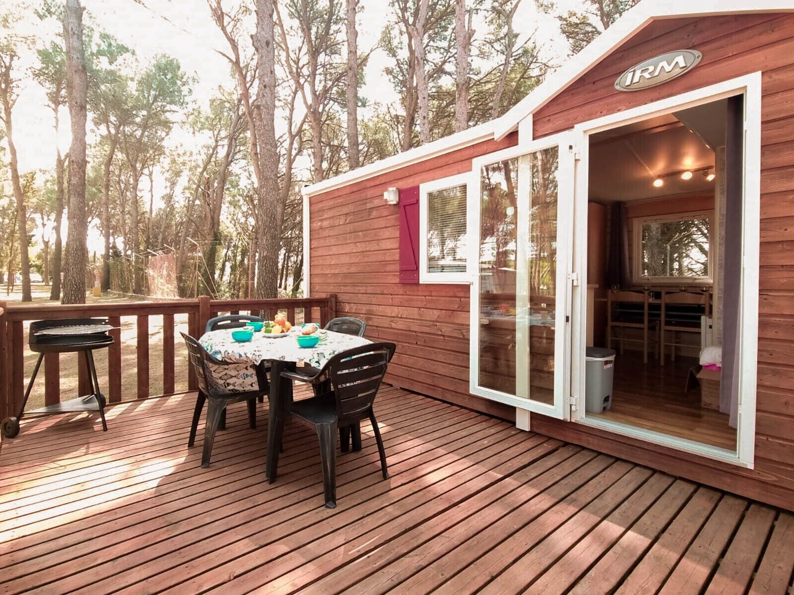 Une terrasse en bois avec une table et des chaises, un barbecue et un bâtiment doté d’une porte coulissante.