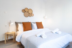 Cama bem arrumada com roupa de cama branca e castanha, luminária de cabeceira e um objeto decorativo fixado na parede.