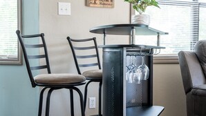 A kitchen area with two bar stools, a black metal bar with a glass shelf, a potted plant, and a wall sign. - Kayaks-Lakefront Home - Kiwanie Lodge West (Hardy)