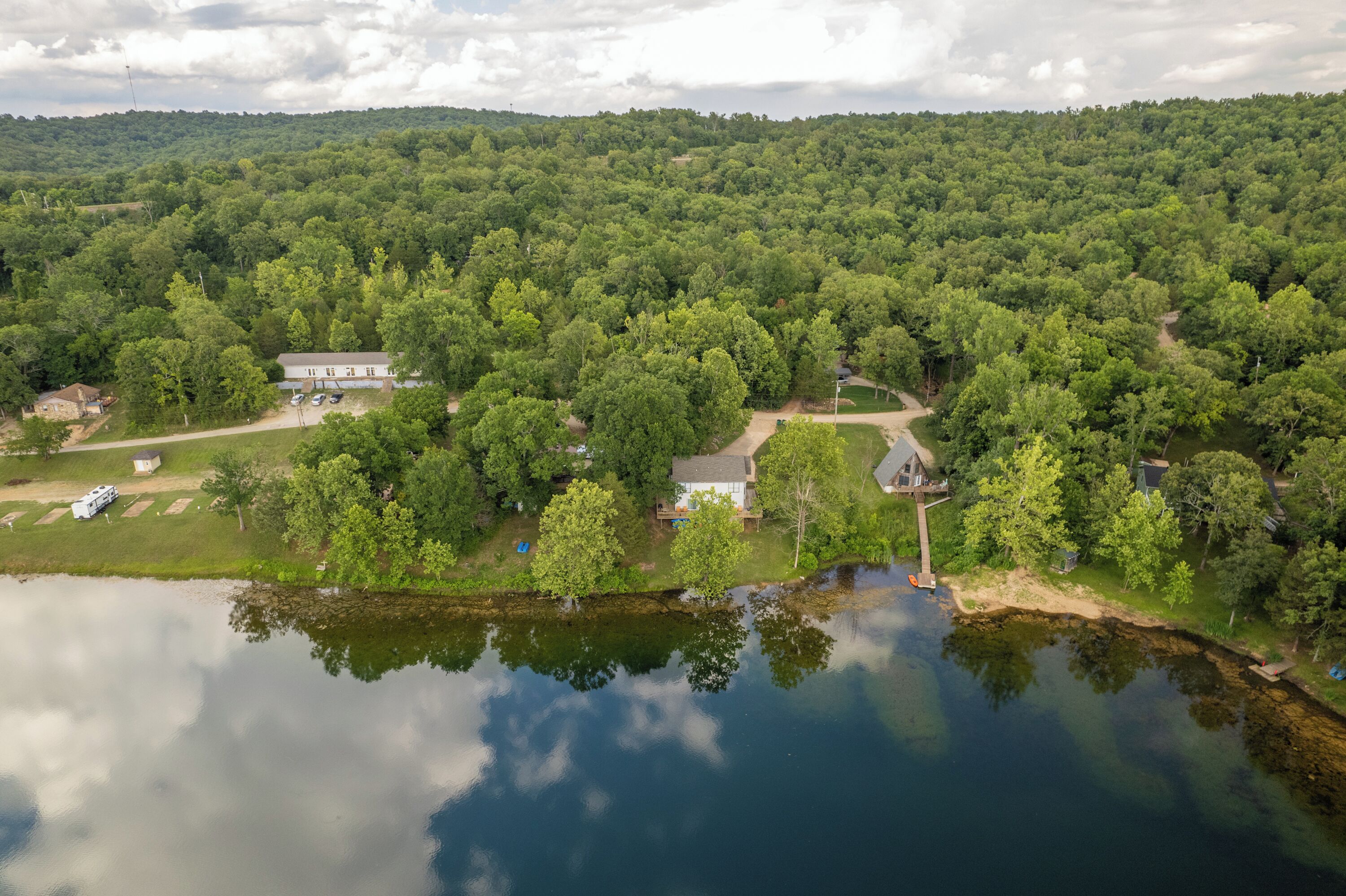 Vue aérienne d’une propriété au bord du lac, comprenant plusieurs bâtiments, un quai et une forêt environnante.