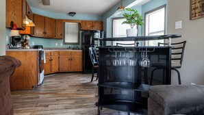 A kitchen with wooden cabinets, a dining area with a black metal table and chairs, and a potted plant on the windowsill. - Kayaks-Lakefront Home - Kiwanie Lodge West (Hardy)