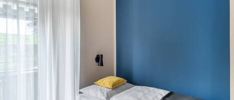 Un dormitorio con cama, ventana con cortinas translúcidas y pared pintada en dos colores.