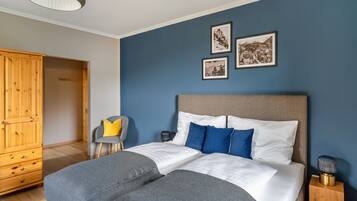 A bedroom with a bed, a wooden wardrobe, a chair, and two framed pictures on the wall.
