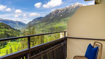 A balcony with a view of a mountainous landscape, a wicker chair with a blue cushion, and a wooden railing.