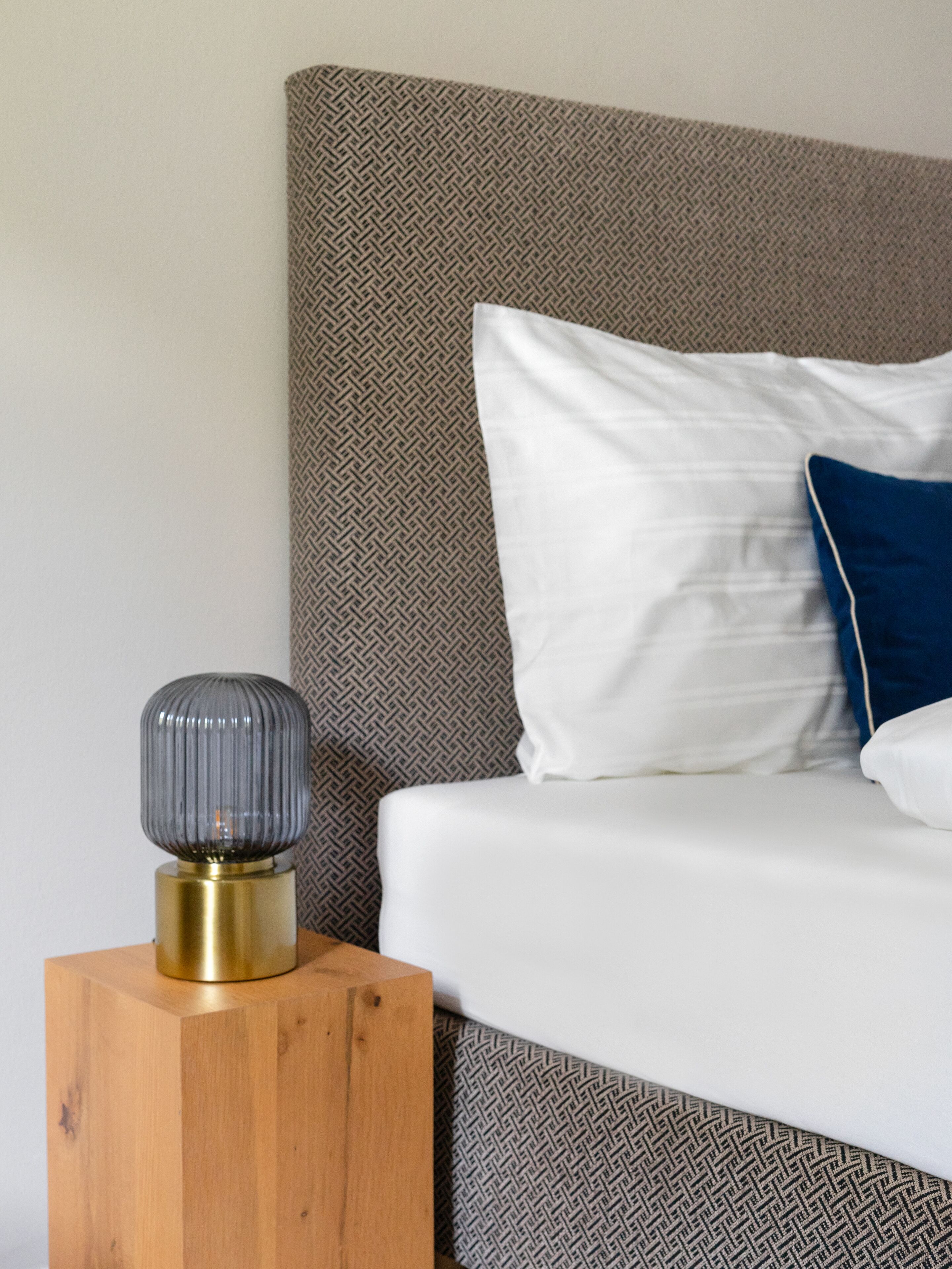 A neatly made bed with a patterned headboard, a bedside table with a lamp, and a wooden nightstand.