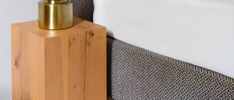 A neatly made bed with a patterned headboard, a bedside table with a lamp, and a wooden nightstand.