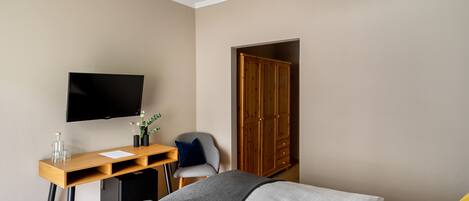 Habitación de hotel con cama, escritorio, televisor de pantalla plana, armario y una silla gris.
