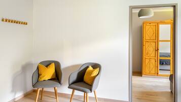 Una habitación con dos sillones grises con cojines amarillos, piso de madera y un armario de madera con espejo.