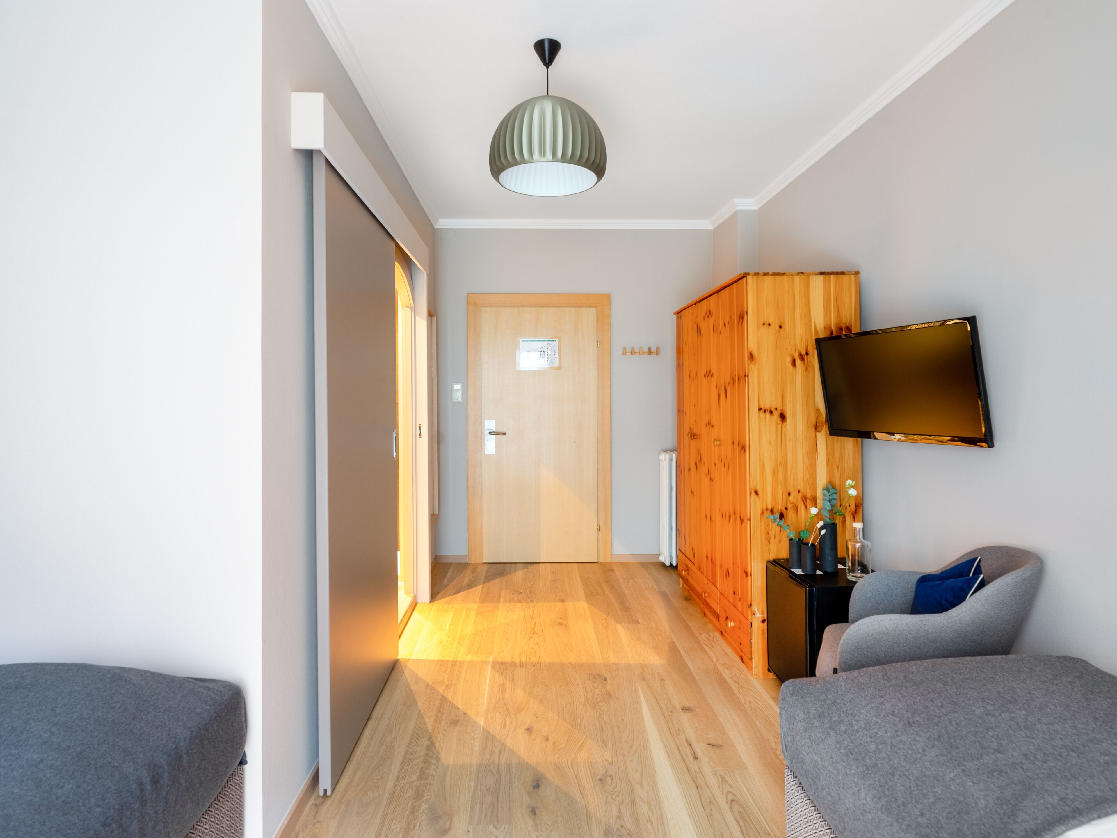 Una sala de estar moderna con piso de madera, un sofá gris, un televisor montado en la pared y un mueble de madera.