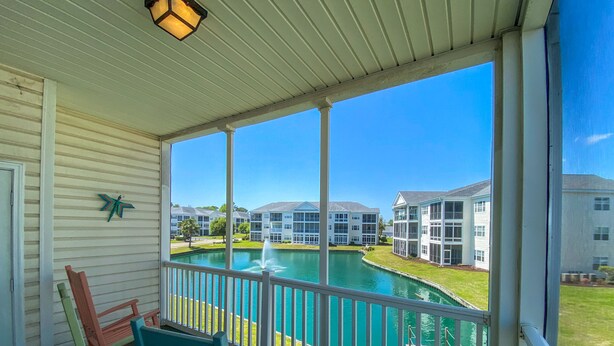 A covered porch with a view of a swimming pool and apartment buildings. - 3 night minimum.  2 bedroom. Outdoor pool. Close to beach. (North Myrtle Beach)