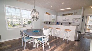 A modern kitchen with white cabinets, a dining area with a round table and chairs, and a view of a parking lot through the window. - 3 night minimum.  2 bedroom. Outdoor pool. Close to beach. (North Myrtle Beach)