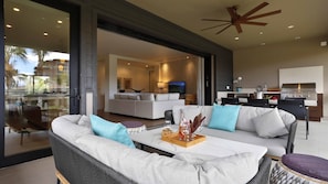 A modern living room with a sofa, coffee table, and dining area. There is a kitchen with a grill and a balcony with a view.