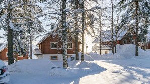 A snow-covered residential area with houses, trees, and a clear sky.
