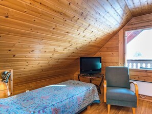 A small, cozy room with wooden walls, a single bed with a patterned bedspread, a television on a small table, and a chair.