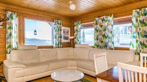 A cozy cabin interior with a sectional sofa, a round coffee table, and a dining table with chairs.