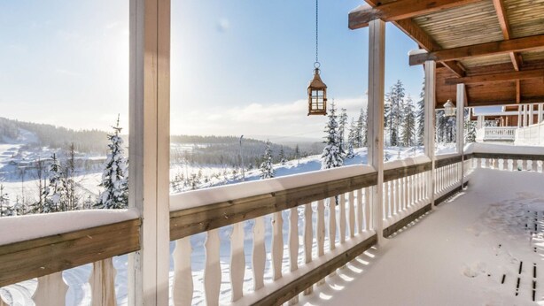 A covered outdoor area with a wooden railing, a hanging lantern, and a snowy landscape with trees in the background.