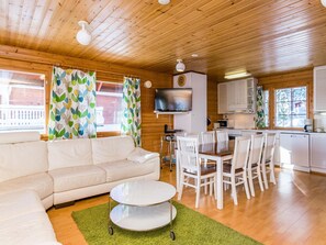 A cozy cabin interior with a sofa, dining table, chairs, a TV, and a kitchen area.