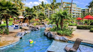 Área de piscina en un resort con tobogán de agua, sillas de descanso y palmeras.