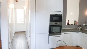 Moderni keittiö, jossa on valkoiset kaapit, sisäänrakennettu uuni ja puinen ruokapöytä.
