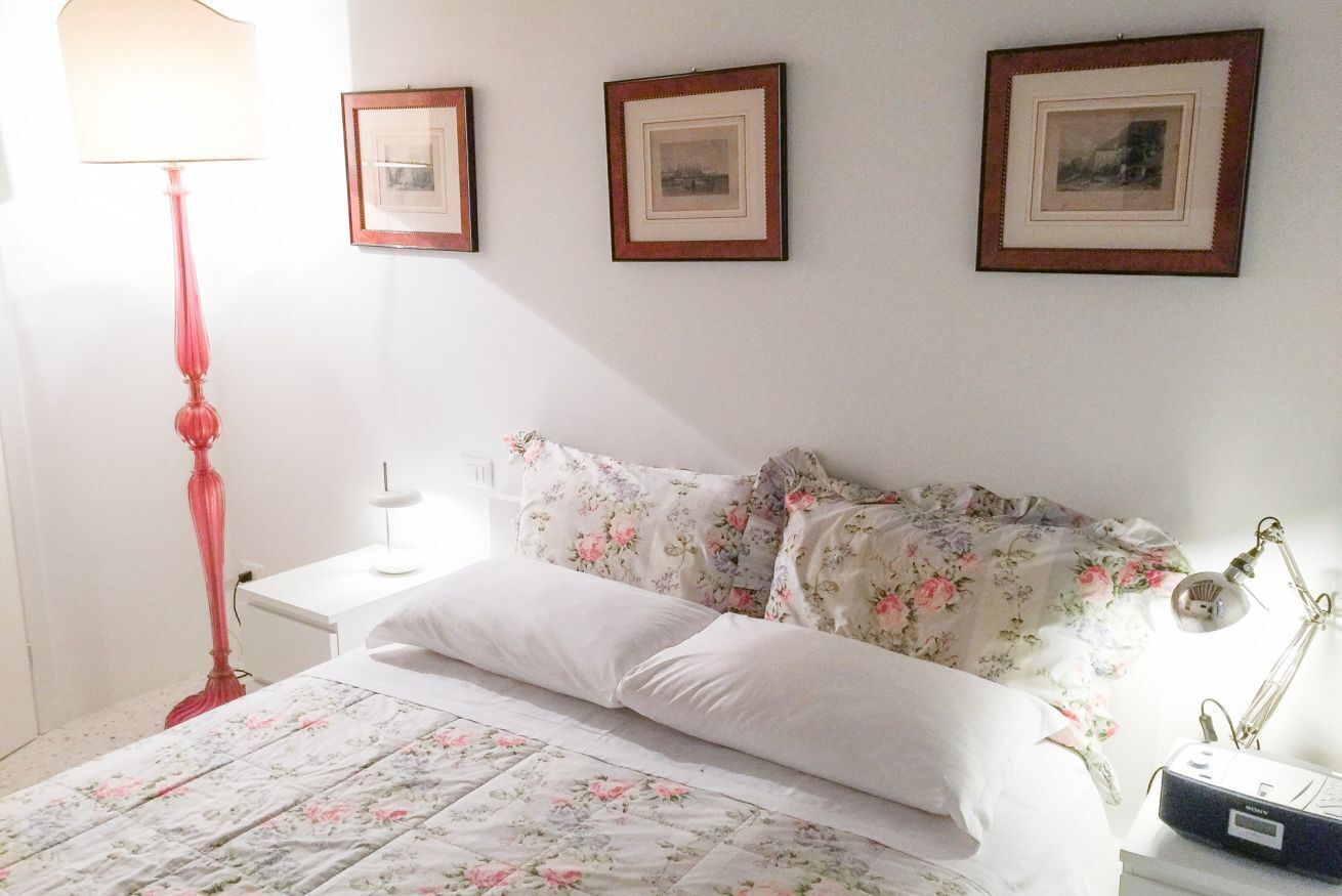 Un dormitorio con cama, mesita de noche, lámpara y tres cuadros en la pared.