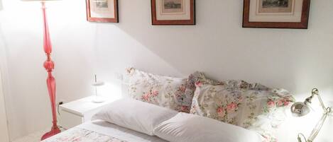 Un dormitorio con cama, mesita de noche, lámpara y tres cuadros en la pared.