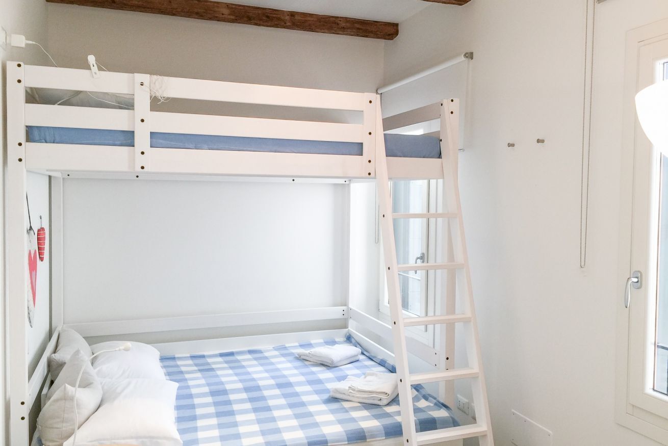 Habitación con literas, una escalera, colcha a cuadros y una ventana.