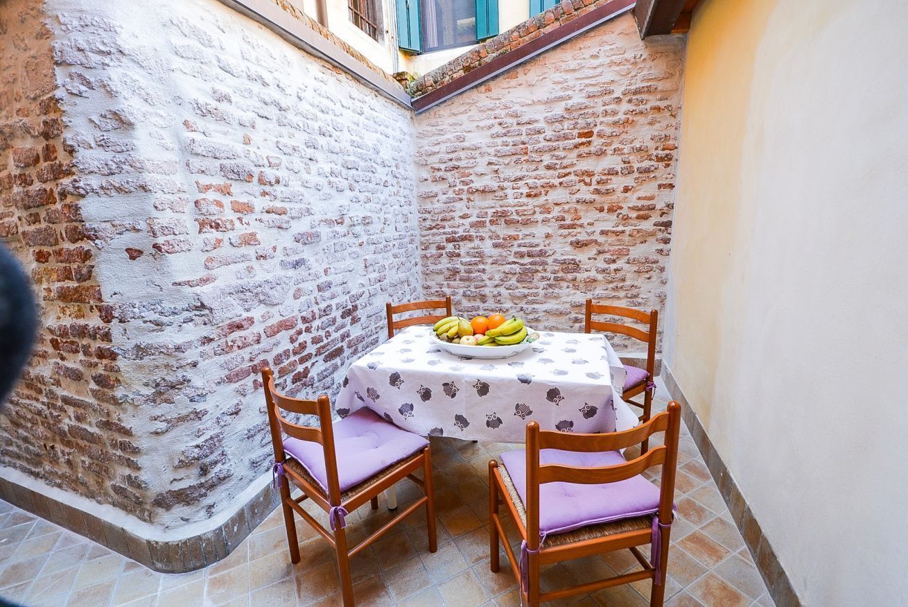 A small, enclosed outdoor dining area with a brick wall, a tiled floor, and a table set with chairs and a fruit bowl.