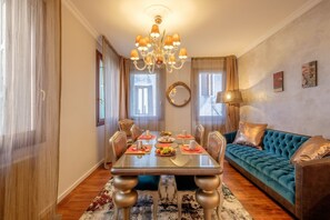 Un comedor con una mesa lista para cuatro personas, rodeada de sillas, una araña y un sofá con cojines.