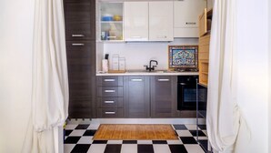 Una cucina compatta con mobili scuri, un pavimento a scacchi bianco e nero e una trave in legno al soffitto.