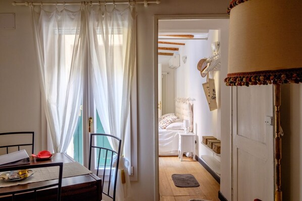Ein Zimmer mit Bett, Nachttisch und einem Fenster mit durchsichtigen Vorhängen.