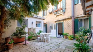 Un cortile con pavimento in pietra, piante in vaso, un tavolo con sedie e una porta con decorazioni a reticolo.