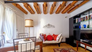 Un soggiorno con soffitto in legno, un divano con cuscini rossi e bianchi, un televisore e una libreria.