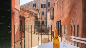 Ein Balkon mit einer Weinflasche und Gläsern auf einem weißen Tisch, mit Blick auf eine enge Straße und Häuser.