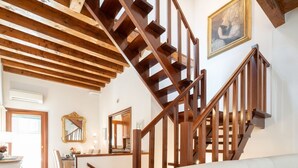 Eine Holztreppe mit Blick auf den darunterliegenden Wohnbereich, ein Spiegel und ein Gemälde an der Wand.