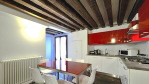 Een moderne keuken met witte kasten, een rode achterwand en een houten plafond. Er staat een eettafel met witte stoelen.