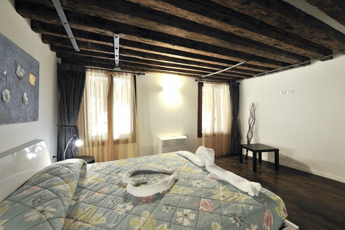 A hotel room with a bed, a bedside table, a chair, a lamp, and a window with curtains.