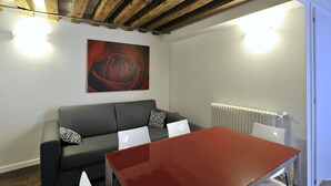 Een moderne kamer met een houten plafond, een zwarte leren bank met twee laptops, een rode tafel en een groot abstract schilderij.