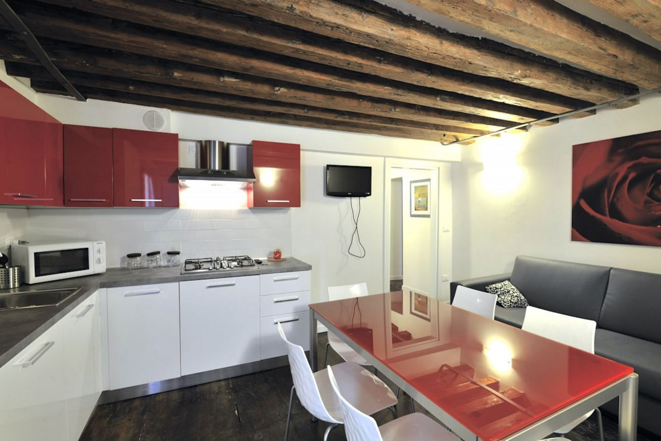 Una cucina moderna con mobili bianchi, un piano di lavoro rosso e un tavolo da pranzo in vetro.