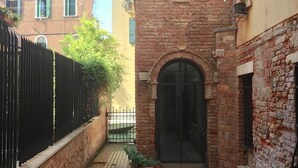 Une ruelle étroite bordée d’un bâtiment en briques, d’un portail en métal noir et d’un pot de fleurs.