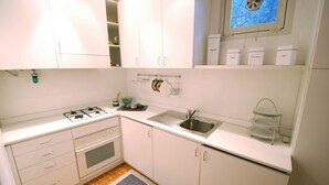 Une cuisine compacte avec des meubles blancs, une cuisinière à gaz, un évier et une fenêtre offrant une vue agréable.