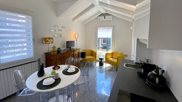 A modern kitchen with a black kettle, a dining area with a white table and clear chairs, and a living area with yellow sofas. - Santa Maria Formosa-Sunny Terrace! Near Rialto and St.Mark's (Venezia)