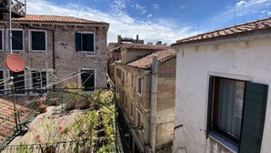 A narrow street with buildings featuring traditional architecture, a small garden area with potted plants, and a clear blue sky. - Santa Maria Formosa-Sunny Terrace! Near Rialto and St.Mark's (Venezia)