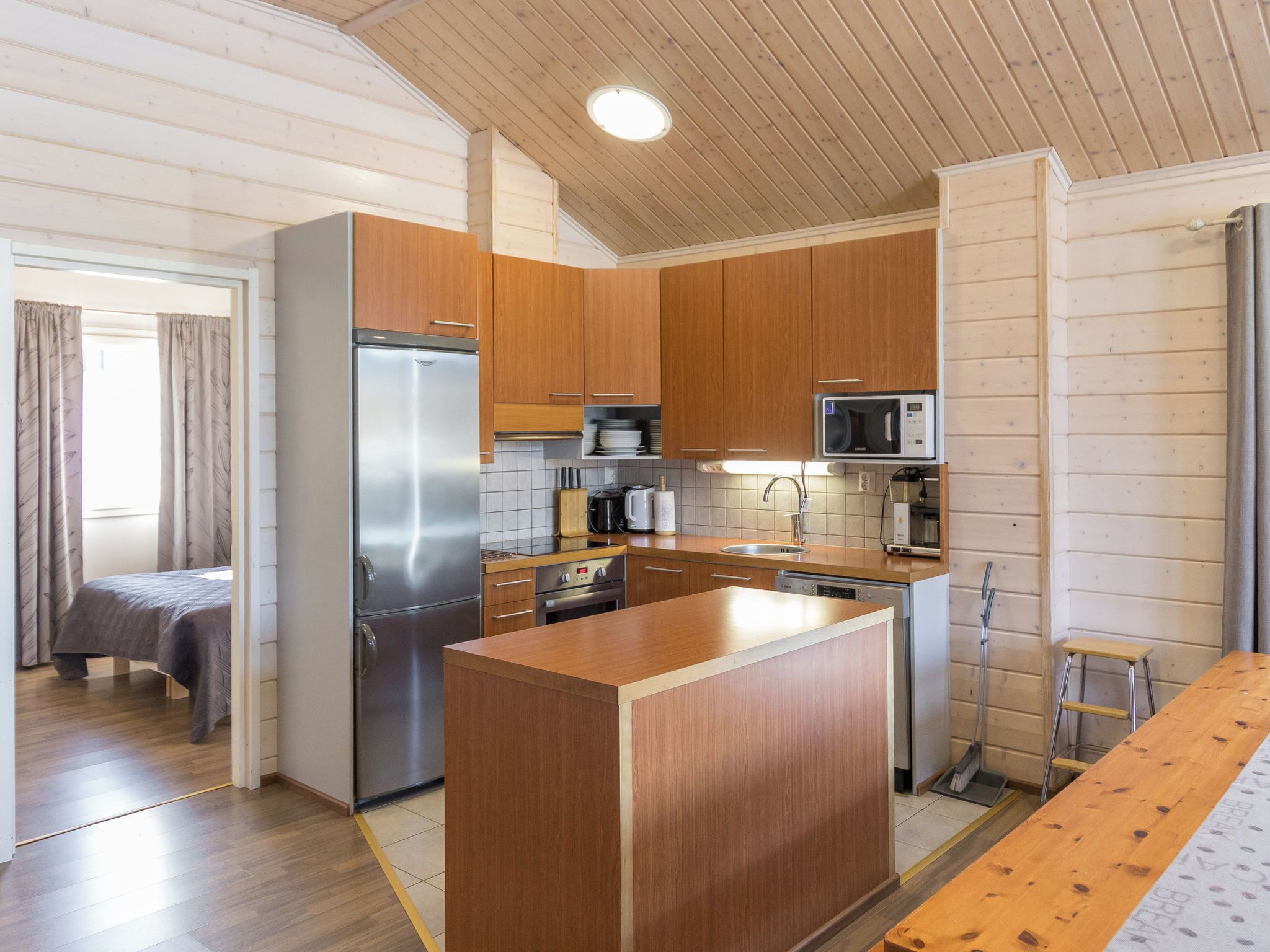 A compact kitchen with wooden cabinets, a stainless steel refrigerator, a microwave, and a dishwasher.