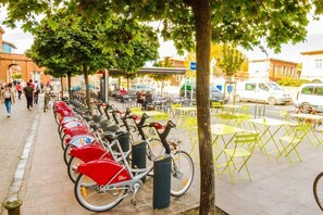 Une rangée de vélos est stationnée le long d’un trottoir, à proximité de tables et de chaises.