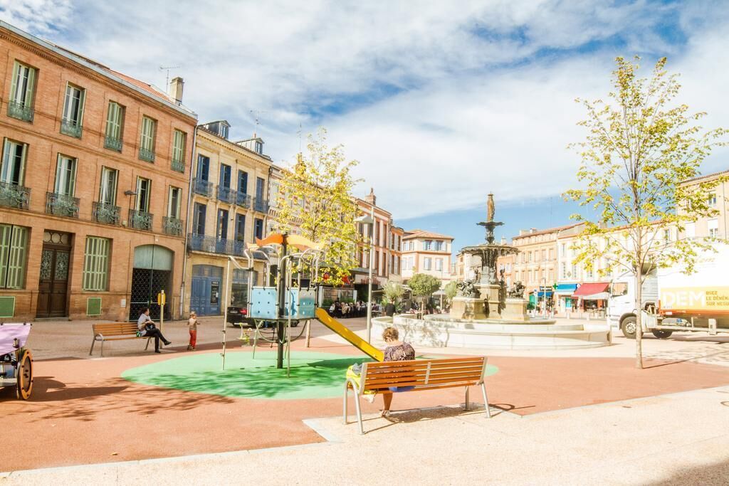 Une place publique avec une aire de jeux, des bancs et une fontaine.