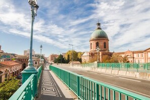 Un pont doté de garde-corps verts et une route menant à un bâtiment surmonté d’un dôme.
