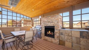 Eine Terrasse im Freien mit Kamin aus Stein, Holzbalkendecke und großen Fenstern.