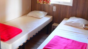 Un alojamiento pequeño de una sola habitación con dos camas, una ventana con cortinas y estanterías empotradas.