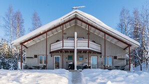 Una cabaña de madera grande con un balcón, rodeada de árboles cubiertos de nieve.